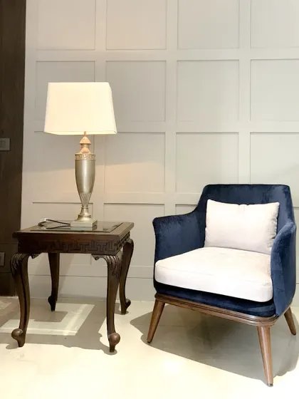 This vignette demonstrates our principle of balancing classic and modern elements. A contemporary armchair in rich blue velvet is paired with an intricately carved wooden side table, creating a harmonious dialogue between two distinct styles.