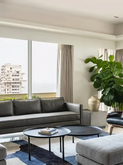 The living room of Apartment 1600, a bachelor pad with panoramic views of the Arabian Sea. The design pays homage to mid-century modern style, with clean-lined furniture, a cool color palette, and large plants that add a touch of tropical luxury.