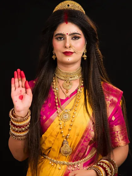 This full-length portrait of Skandamata shows the complete styling, from the hair and makeup to the traditional yellow and pink saree.