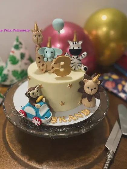 A whimsical party animal cake where a monkey drives a car. This fun design features a giraffe, elephant, zebra, and lion all wearing party hats for a 3rd birthday.