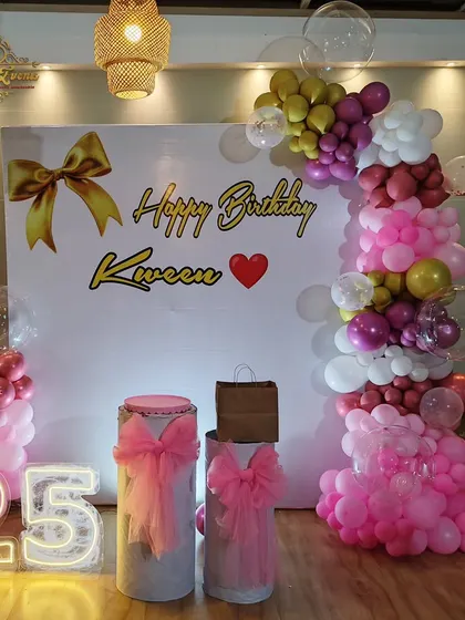 A chic 25th birthday setup with a custom backdrop, an organic pink balloon garland, and large light-up numbers.