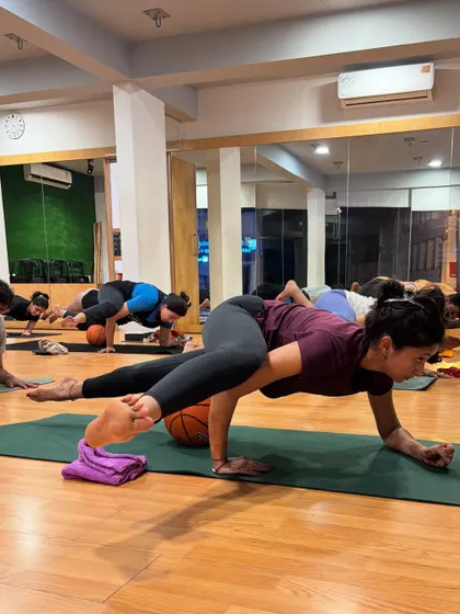 An advanced arm balance pose, with a student using a basketball for support and challenge.