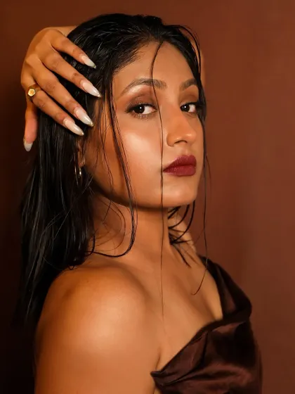 A close-up of the sultry, wet-look makeup. The glossy skin and hair, paired with a deep berry lip, create a high-fashion, edgy vibe.