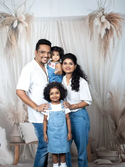 A happy family of four, dressed in coordinated white shirts and denim, sharing a genuine, joyful moment in the studio.