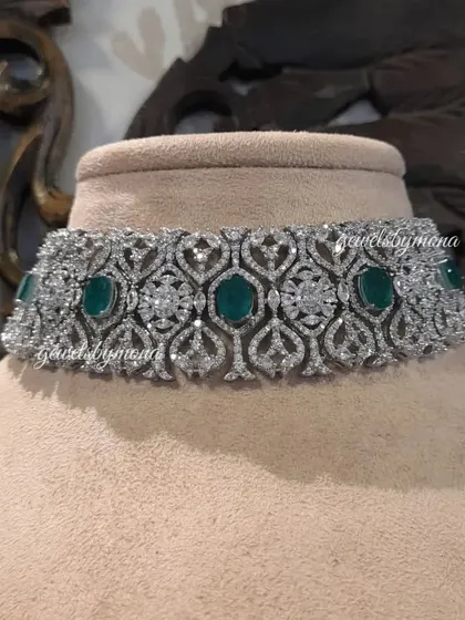 A close-up of a stunning diamond and emerald choker. The design features a beautiful pattern of pavé-set diamonds interspersed with rich, oval-cut emeralds, creating a piece that is both classic and luxurious.