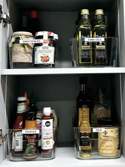 Clear bins are perfect for organizing oils, sauces, and sweeteners in a kitchen cabinet. This method of 'containing' keeps bottles from tipping over and makes it easy to pull out a whole category at once.