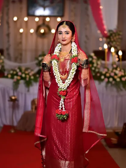 A full-length shot of the bride on her wedding day, looking regal in her red saree and veil.