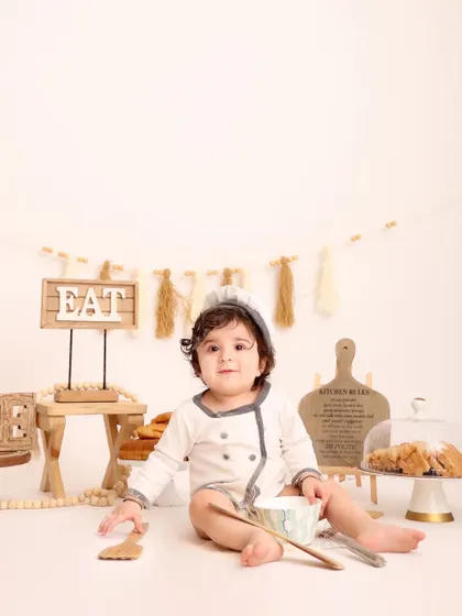 A quiet moment for the little chef. This portrait captures the baby sitting calmly amidst the baking setup, looking directly at the camera with a sweet expression.