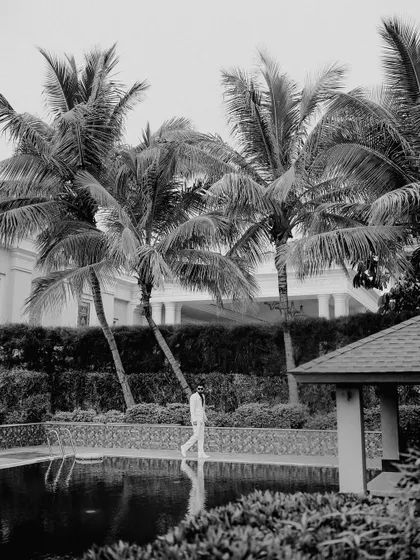 A minimalist black and white shot of the groom by the pool. The reflection in the water and the strong lines of the palm trees create a stylish and artistic composition.