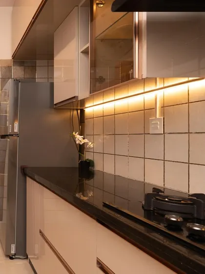 This modular kitchen from a Bangalore home tour features warm under-cabinet lighting, a black granite countertop, and a mix of open and closed storage.