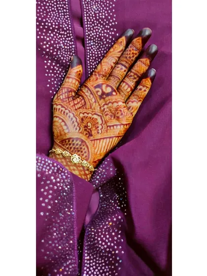 A rich henna stain on the palm, set against a beautiful purple fabric. The design combines traditional Indian mehndi patterns for a full and festive look.