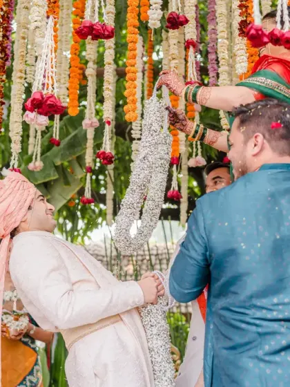 The groom playfully struggles as the bride tries to place the garland on him during the varmala ceremony. This action-packed, fun moment is a highlight of many Indian weddings.