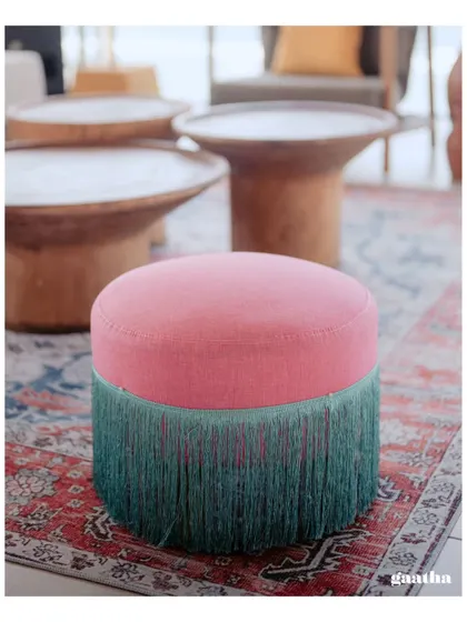 A vibrant pink and teal fringed ottoman, adding a pop of color and texture to the lounge area at a tropical-themed event.