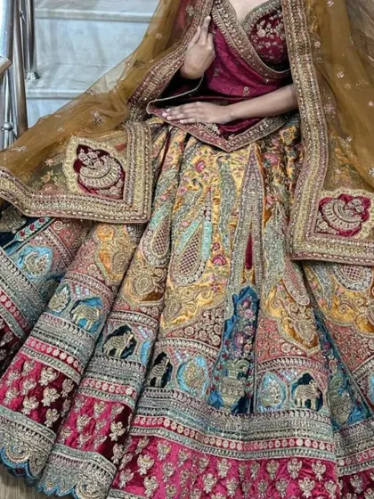 Look at the craftsmanship on this multi-colored velvet lehenga. The skirt is decorated with detailed elephant and peacock motifs in panels, giving it a very traditional and regal feel. This is a heavy bridal piece for the main event.