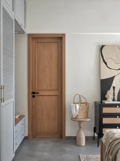 This master bedroom was tailored exactly to the client’s vision of a tranquil haven. The combination of grey louvered wardrobes, a black and cane chest of drawers, and a warm wooden door creates a balanced and serene space.