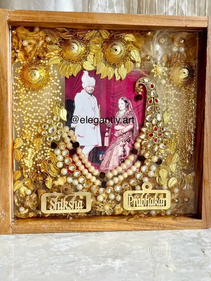 A close-up view of a magnificent teakwood frame preserving a couple's wedding photo, varmala, and kalgi. The intricate details and golden name tags make this a truly royal keepsake.
