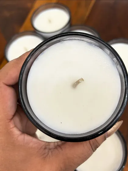 A close-up of a simple, elegant scented candle in a black glass jar. I can customize the fragrance, color, and jar for any occasion.