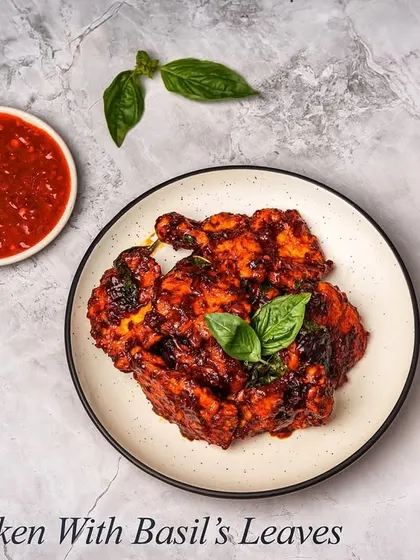 An overhead shot of our Crispy Chicken with Basil, served with a side of spicy red sauce and chopped garlic. This dish offers a perfect combination of crunchy texture and aromatic flavors.