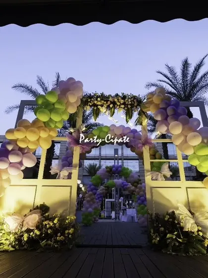 The butterfly-themed entrance arch at dusk. The lighting on the balloons and the giant butterfly cutout creates a dramatic and beautiful welcome.