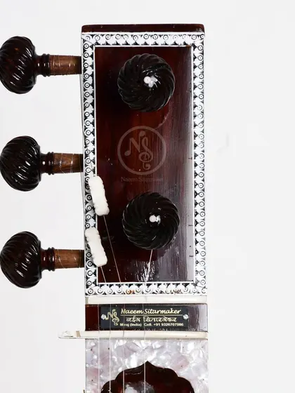 The headstock of an Ustad Vilayat Khan style sitar, showing our maker's mark. The carved pegs are made from rosewood for durability and a good grip.