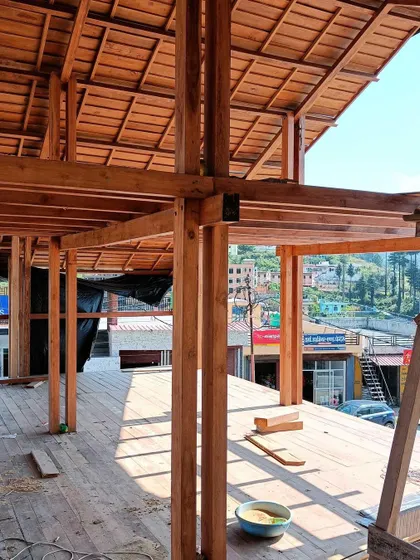 **Market Plaza, Champawat:** An interior view of the exposed wooden structure, showing the beams and columns that define the space. The open-air design provides views of the surrounding town and hills.