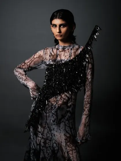 A full-body shot showcasing the complete avant-garde look. The sleek hair and dramatic makeup work together with the textured, abstract dress to create a cohesive and futuristic fashion statement.