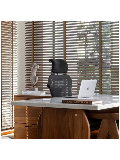 A close-up of the director's desk, where a marble top meets a warm wood base. Wooden blinds control the natural light, and a sculptural piece adds an artistic touch, reflecting a space designed for a leader.