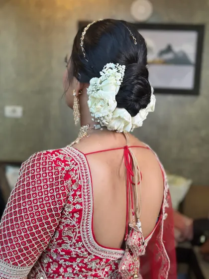 A full and voluminous bridal bun decorated with white roses and baby's breath. This is a timeless wedding hairstyle that pairs beautifully with a traditional red lehenga and gold jewellery.