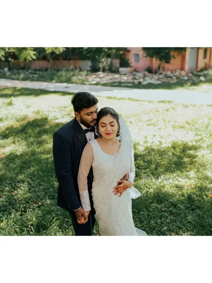 An intimate embrace in a green meadow. The groom holds his bride, who is dressed in a beautiful white lace saree-style gown, creating a serene and romantic portrait.