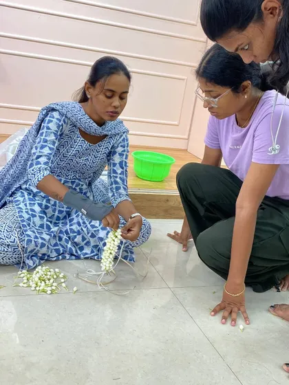A trainer guiding a student through the delicate process of jasmine garland making.