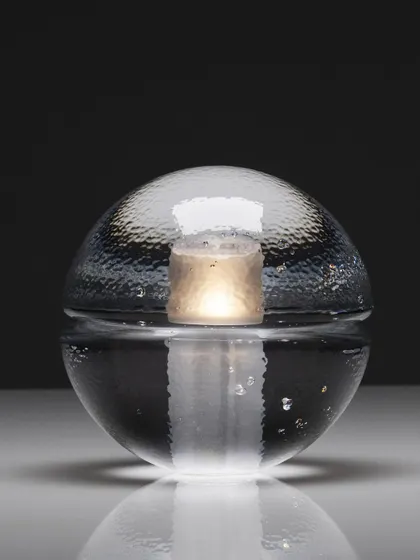 A studio shot of the clear glass 14p, its internal light source creating a beautiful, watery reflection on the surface below.