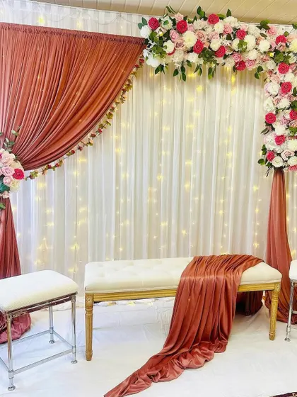 I love playing with unique color combinations, like the warm rust drapes paired with soft pink and white flowers in this setup. The asymmetrical floral arch adds a modern touch, while the fairy lights in the background give it a magical glow. This is a great option for a chic and stylish pre-wedding event.