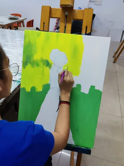 The initial blocking stage of an acrylic painting, where the student lays down the background colors before adding the central figure.