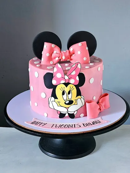 A classic Minnie Mouse cake, perfect for a "twoddler's" party. The design features Minnie's iconic polka-dot bow and a hand-painted character portrait on a pink whipped cream base.