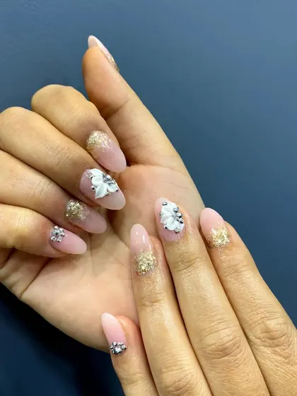 A beautiful hand-posed shot of the gel and acrylic nail demonstration set, highlighting the 3D white flowers and gold glitter accents.