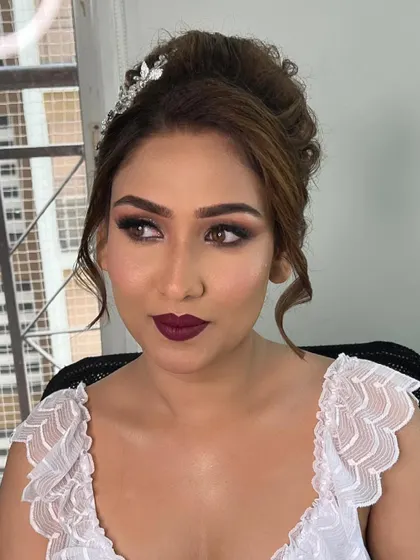 A glamorous Christian bride adorned in wine hues. The look features dramatic sparkle on the eyes and a bold lip, paired with a romantic, curly updo.