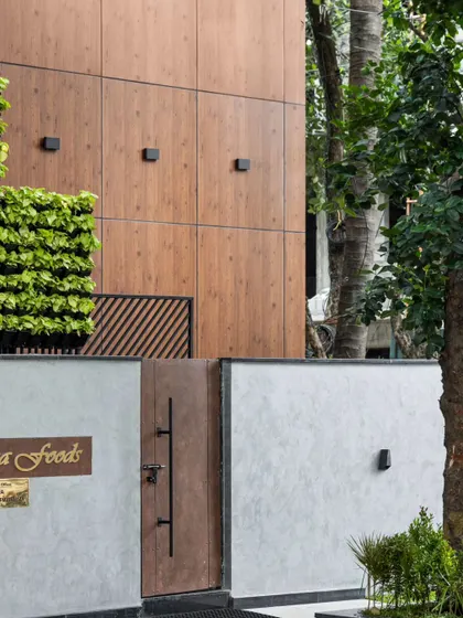 A detail of the Meghana Foods office entrance, where a vertical garden contrasts with the clean lines of the wood-paneled facade and concrete wall. The design uses texture and natural elements to create an inviting and memorable entryway.