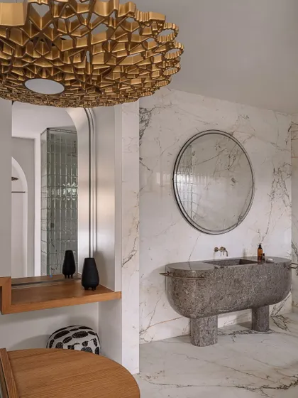 This walk-in wardrobe and ensuite bathroom was designed to feel like a chic SoHo store. It features a sculptural monolithic marble basin and a dramatic golden light fixture.