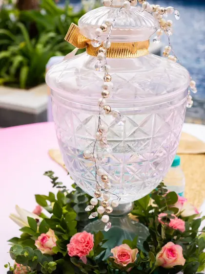 A beautiful crystal beverage dispenser adorned with pearls and surrounded by fresh flowers. This is an elegant way to serve drinks at a sophisticated event.