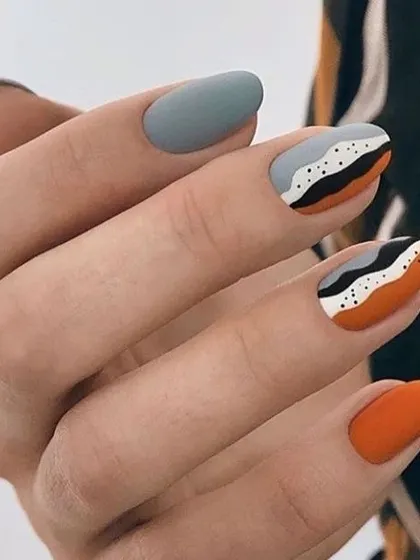 This design showcases the beauty of matte finish nail art. It combines solid orange and grey nails with an abstract pattern in black, white, and orange for a sophisticated, textured look.