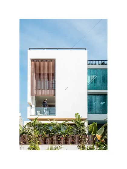 The facade of the Notan Home features a mix of materials and textures, including smooth white plaster, wooden screens, and vibrant blue jaali walls. These elements work together to create a visually rich exterior that changes with the light throughout the day.