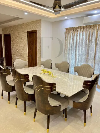 An eight-seater dining table with a pristine white onyx top and a dark wood base. The chairs are upholstered in a rich, patterned fabric with elegant gold inlay, creating a truly luxurious dining experience.
