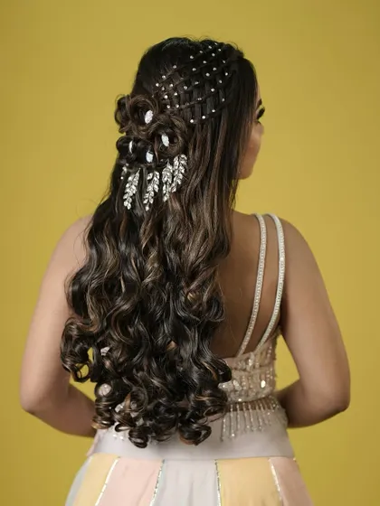 A glamorous half-updo with intricate weaving, hair roses, and sparkling crystal accessories. This is a show-stopping look for a reception or sangeet.
