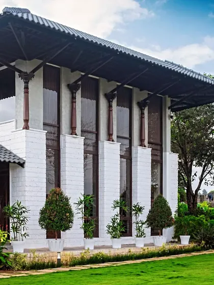 The facade of the classical farmhouse, with its tall columns and potted topiary, stands proudly amidst the green landscape.