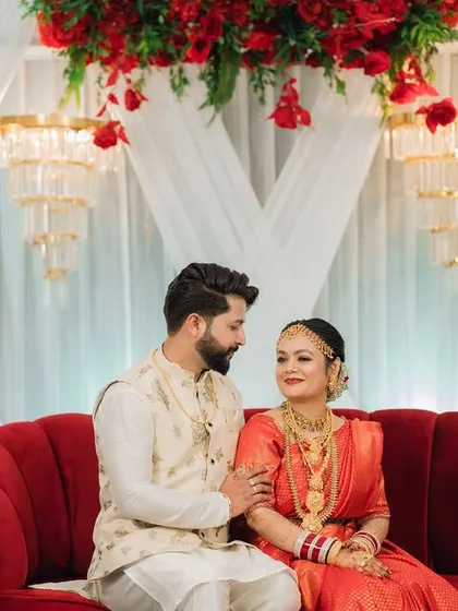 A sweet moment between the couple on their wedding stage, which features a bold red sofa and an elegant white and red floral decor theme.