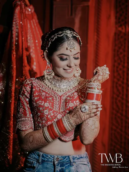 A fun and modern bridal shot. The bride pairs her traditional red choli and heavy jewelry with a pair of blue jeans, showing her unique style and joyful spirit while getting ready.