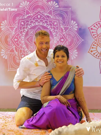 A happy portrait from the Haldi ceremony. The couple, covered in turmeric, smiles against a backdrop of colorful mandala art, perfectly capturing the fun and festive spirit of the day.