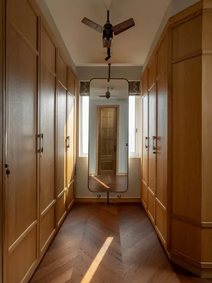 A walk-in closet in the Aalay residence, where natural light from flanking windows illuminates the warm wood cabinetry. We designed this space for function and flow, with a full-length mirror that enhances the sense of depth and utility.