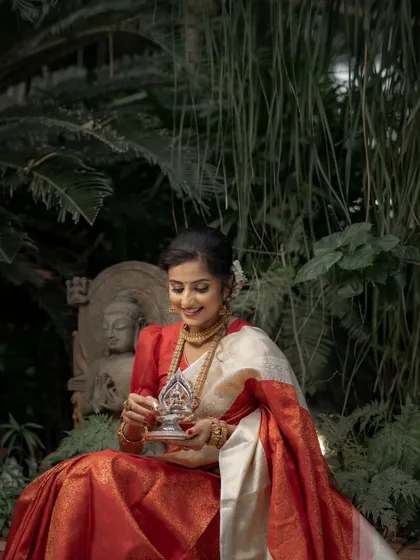 The gentle light and lush background highlight the beauty of the bride and her traditional red saree, a classic choice for any South Indian wedding.