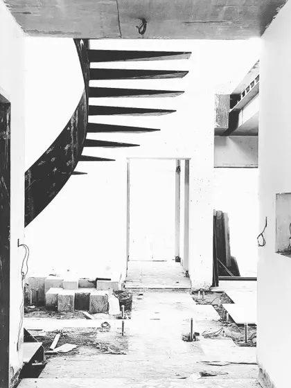 A black and white photo of the helical staircase during construction. The raw steel form stands as a powerful sculptural element within the unfinished space.